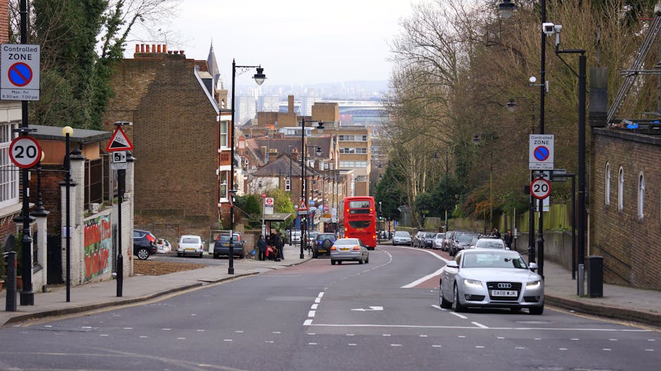 A street scene on Stoke Newington Church Street in Stamford Hill with a view of residential buildings and commercial signage. Parked cars are aligned along both sides of the road, including a silver A